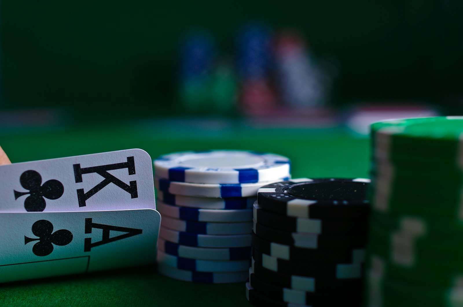A hand holding four playing cards beside stacks of poker chips on green felt